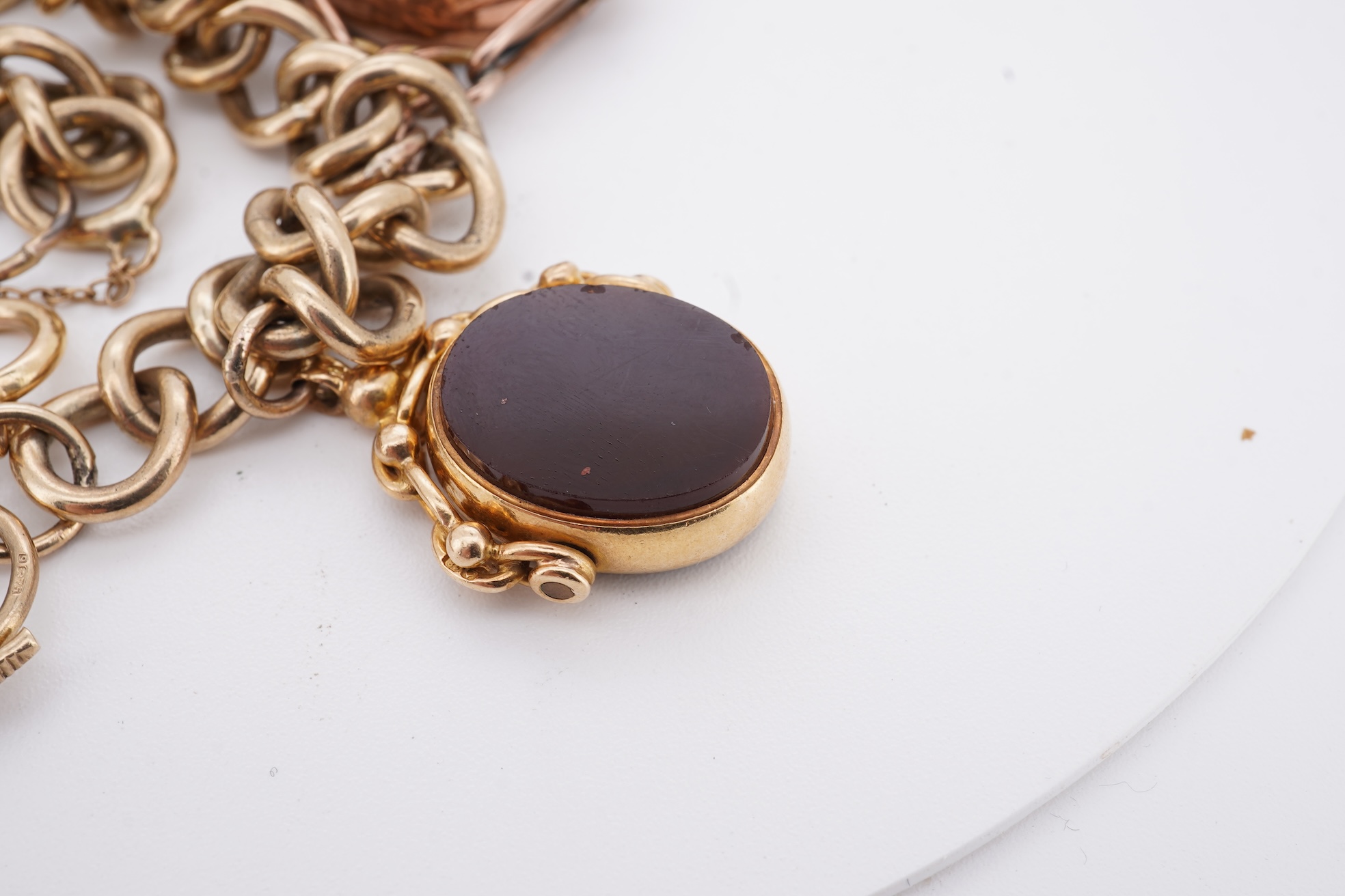 A 1970's 9ct gold curb link charm bracelet, with 9ct gold heart shaped clasp, hung with seven assorted gold or gilt metal mounted charms including six chalcedony set fob seals, gross weight 73 grams.